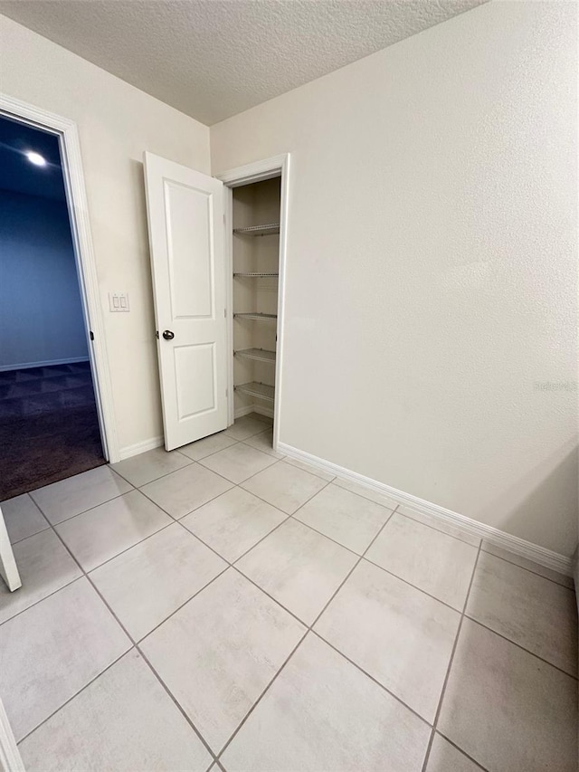 unfurnished bedroom featuring light tile patterned floors, a textured ceiling, a closet, and baseboards