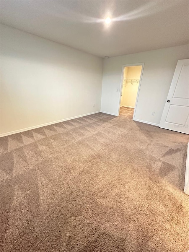 unfurnished bedroom featuring a walk in closet, baseboards, carpet, and a closet