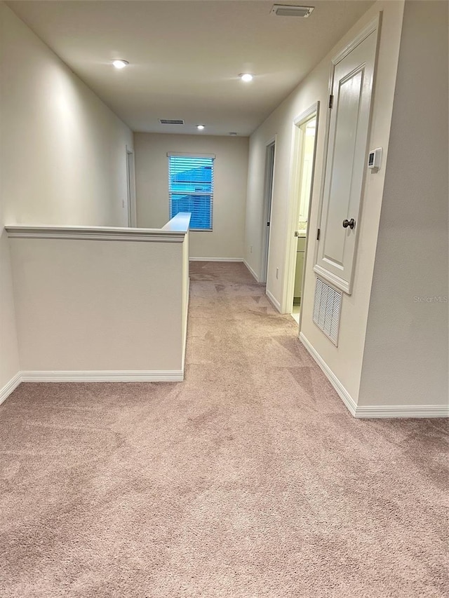 hallway featuring baseboards, visible vents, and light carpet