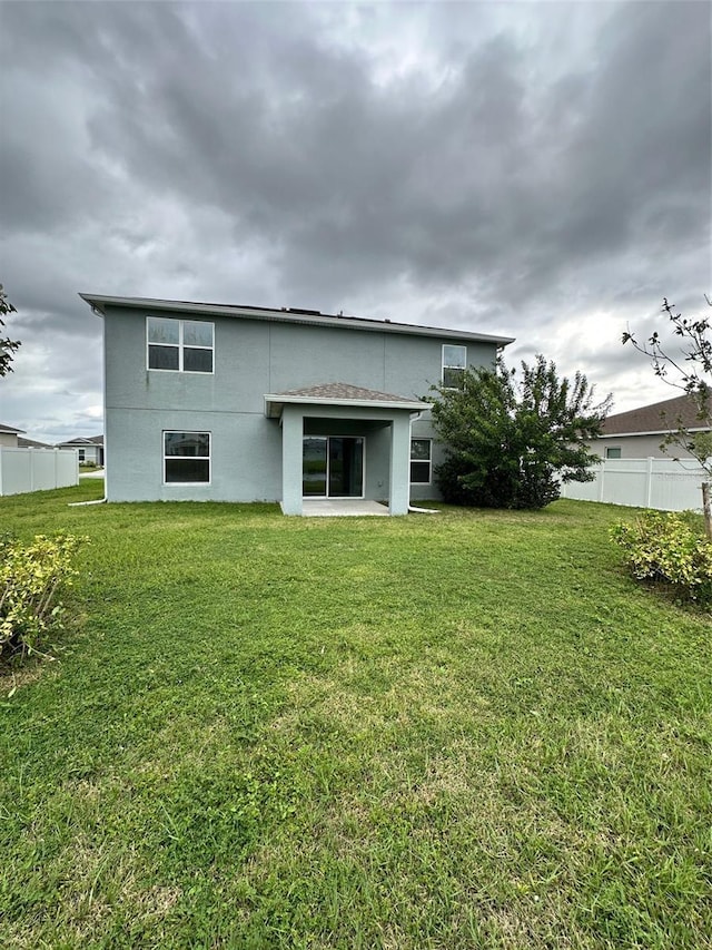 back of house featuring stucco siding, fence, and a lawn