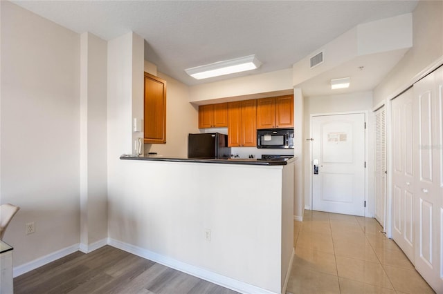 kitchen with light wood-type flooring, black appliances, kitchen peninsula, and a textured ceiling