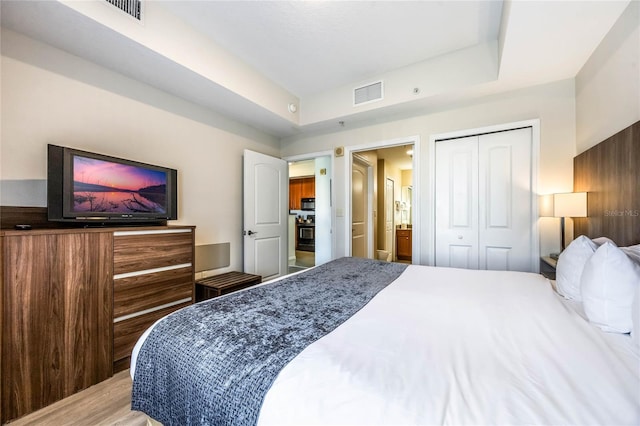 bedroom with a raised ceiling, light hardwood / wood-style flooring, and a closet