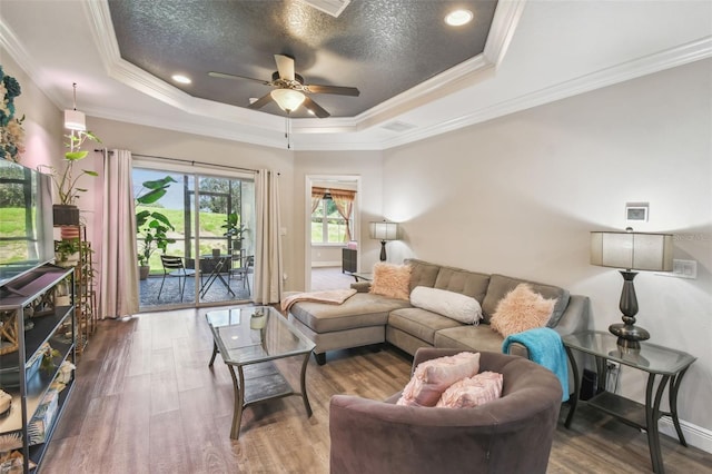 living room featuring ceiling fan, a raised ceiling, dark wood-type flooring, and ornamental molding