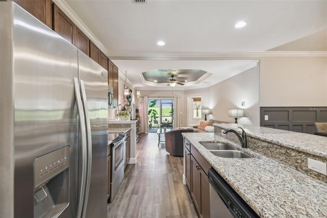 kitchen with dark wood-type flooring, a raised ceiling, stainless steel appliances, ceiling fan, and sink