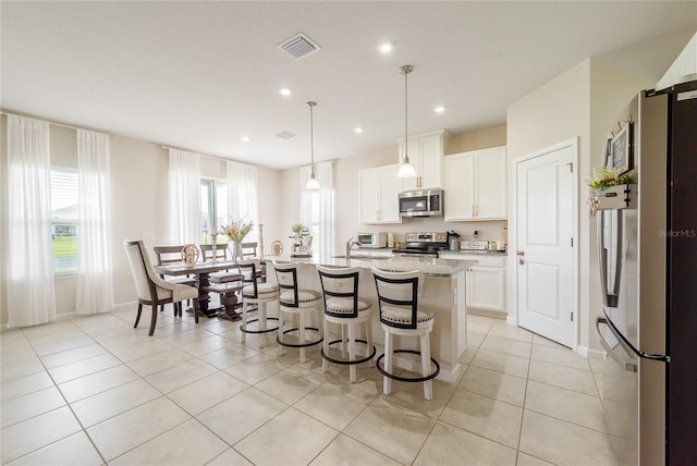 kitchen featuring light stone countertops, a kitchen island with sink, stainless steel appliances, white cabinets, and decorative light fixtures