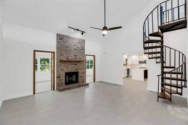 unfurnished living room with a fireplace, a high ceiling, track lighting, and a healthy amount of sunlight