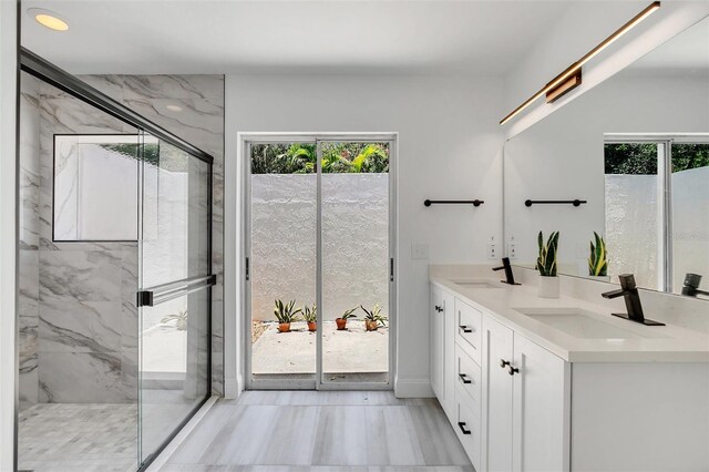 bathroom with vanity, a shower with shower door, and a healthy amount of sunlight