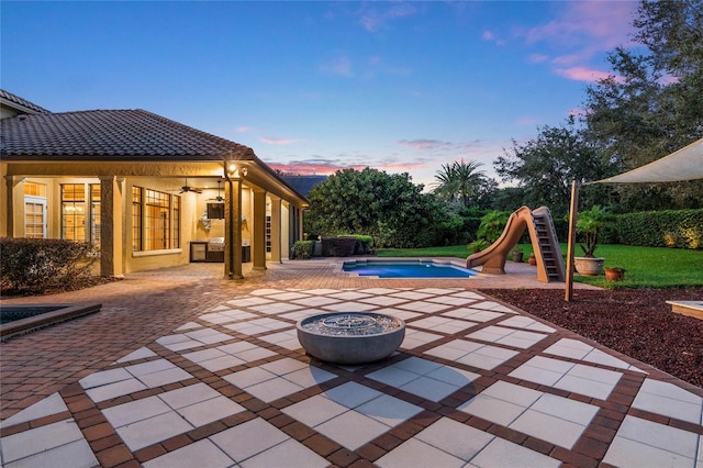 patio terrace at dusk with a swimming pool with hot tub and a fire pit