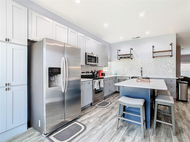 kitchen with appliances with stainless steel finishes, gray cabinetry, a kitchen breakfast bar, a center island, and light hardwood / wood-style flooring