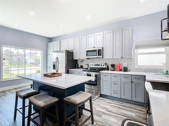 kitchen with light hardwood / wood-style flooring, a wealth of natural light, appliances with stainless steel finishes, and a breakfast bar area