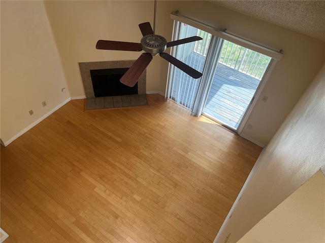 unfurnished living room with ceiling fan, a textured ceiling, a fireplace, and light wood-type flooring