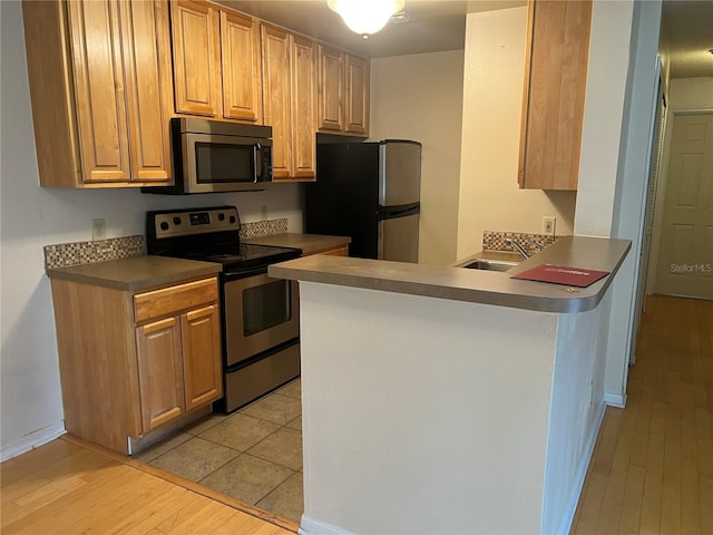 kitchen featuring stainless steel appliances, kitchen peninsula, light wood-type flooring, and sink