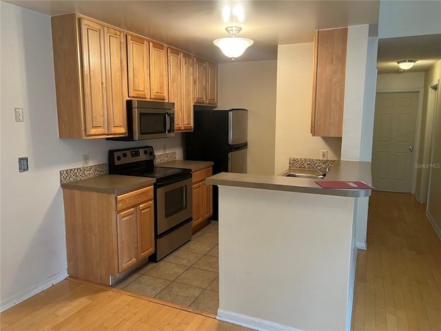 kitchen featuring light brown cabinets, sink, kitchen peninsula, light hardwood / wood-style flooring, and appliances with stainless steel finishes