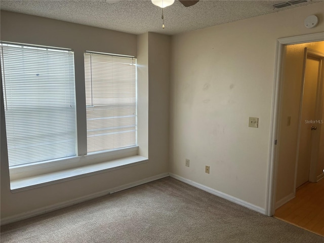 empty room featuring a wealth of natural light, ceiling fan, carpet flooring, and a textured ceiling