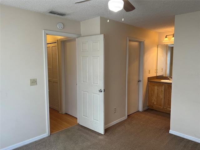 unfurnished bedroom with a textured ceiling, carpet, sink, and ceiling fan