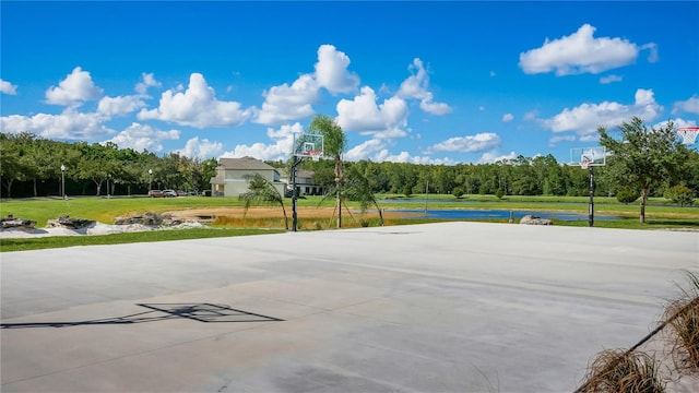 view of sport court with a lawn and a water view