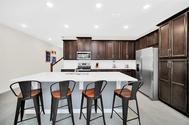 kitchen featuring appliances with stainless steel finishes, dark brown cabinetry, sink, and an island with sink