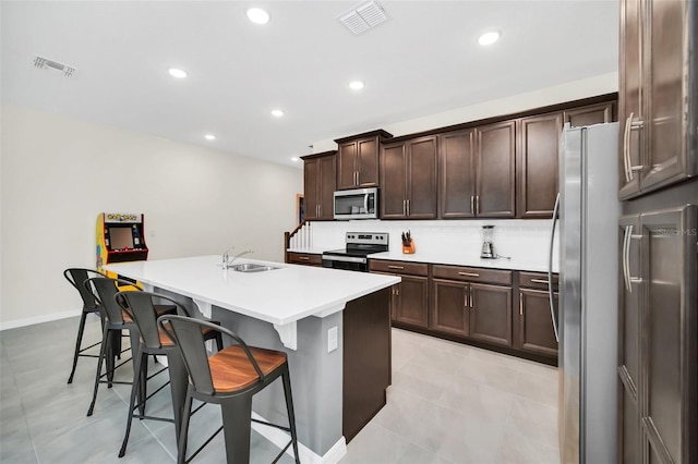 kitchen featuring dark brown cabinetry, sink, a kitchen island with sink, appliances with stainless steel finishes, and a kitchen bar