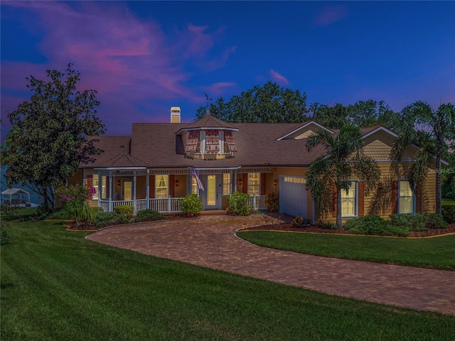 view of front of home featuring decorative driveway, a yard, a chimney, a porch, and an attached garage