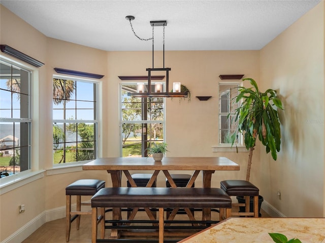 dining space with breakfast area, a chandelier, a textured ceiling, and baseboards