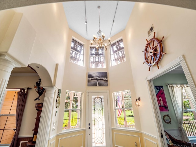 foyer entrance with arched walkways, a notable chandelier, visible vents, a towering ceiling, and decorative columns