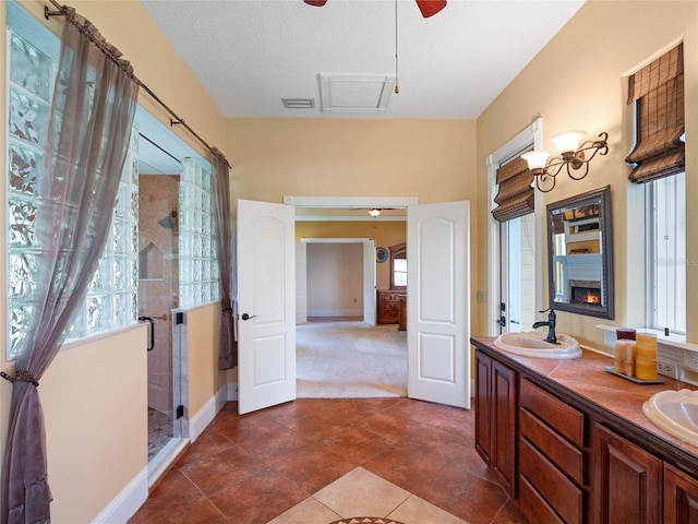 bathroom featuring double vanity, visible vents, a sink, a shower stall, and a warm lit fireplace