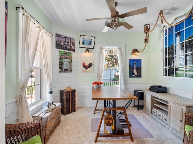 office area with a wainscoted wall, visible vents, a ceiling fan, light carpet, and a textured ceiling