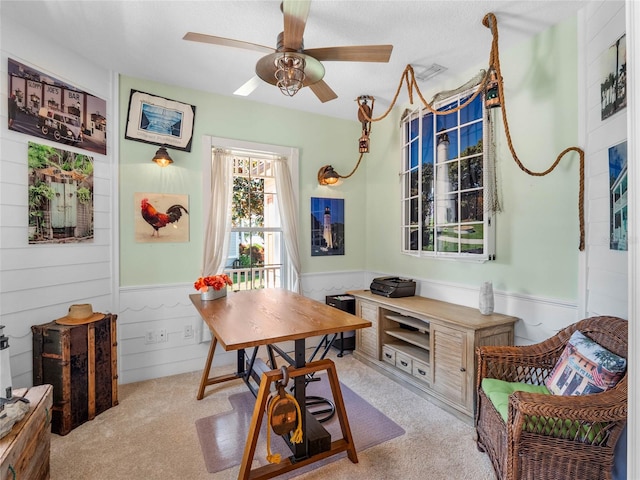 dining room featuring a wainscoted wall, ceiling fan, light carpet, and a textured ceiling