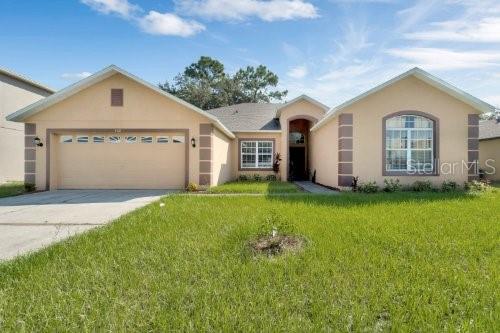 single story home with stucco siding, concrete driveway, a front lawn, and a garage