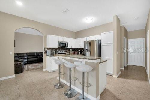 kitchen with a kitchen breakfast bar, an island with sink, white cabinets, light tile patterned floors, and stainless steel appliances