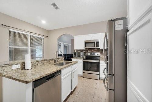 kitchen featuring a kitchen island with sink, a sink, stainless steel appliances, arched walkways, and white cabinets
