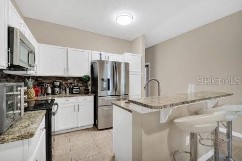 kitchen with light stone counters, white cabinets, backsplash, stainless steel appliances, and a kitchen island with sink