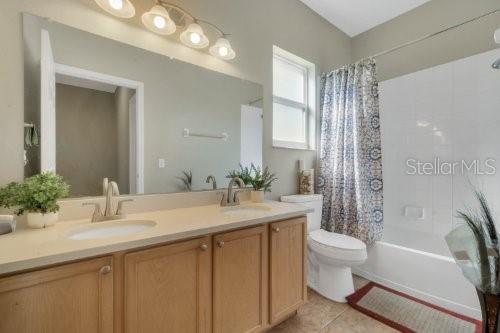 full bathroom with shower / bath combo with shower curtain, tile patterned floors, vanity, and toilet