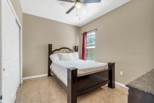 bedroom with light tile patterned flooring, a ceiling fan, a closet, and baseboards