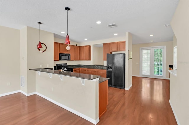 kitchen featuring hanging light fixtures, kitchen peninsula, a textured ceiling, black appliances, and hardwood / wood-style floors