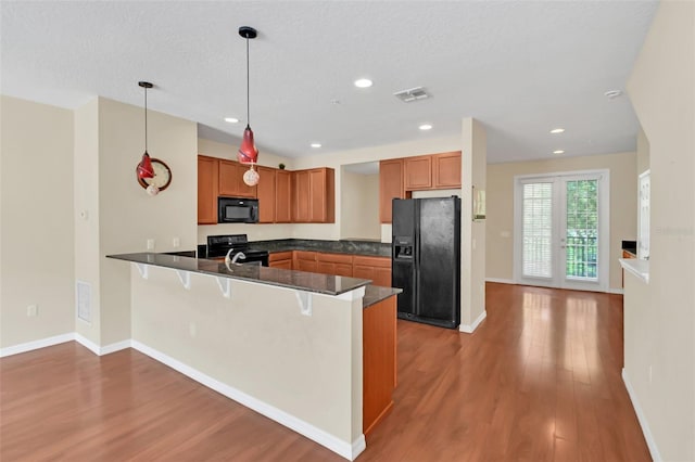kitchen with a peninsula, brown cabinets, dark countertops, visible vents, and black appliances