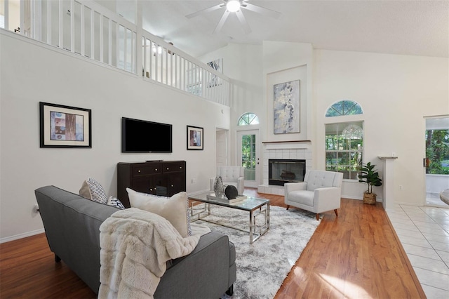 living room featuring high vaulted ceiling, a tiled fireplace, wood-type flooring, and ceiling fan