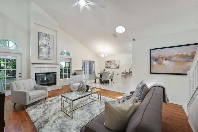 living room with hardwood / wood-style floors, a tiled fireplace, high vaulted ceiling, and ceiling fan with notable chandelier