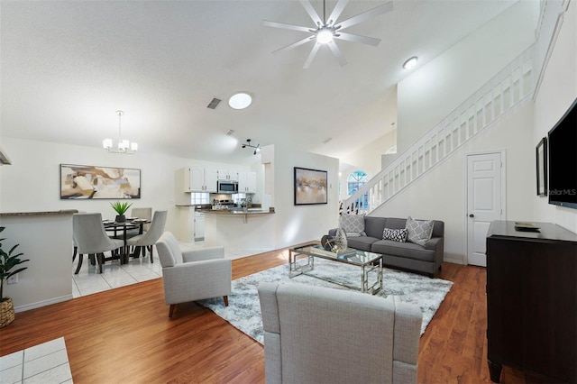 living room featuring ceiling fan with notable chandelier, light wood-type flooring, and lofted ceiling