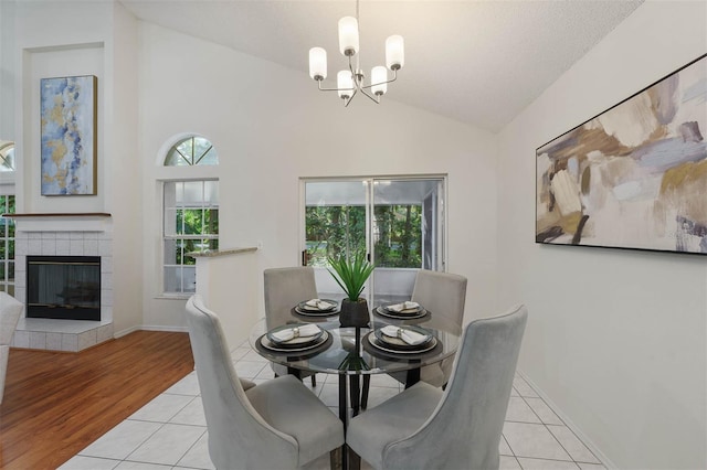 dining area featuring a textured ceiling, a notable chandelier, lofted ceiling, a tile fireplace, and light hardwood / wood-style flooring