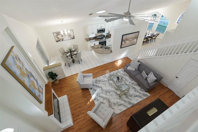 living room with a towering ceiling, ceiling fan with notable chandelier, and light hardwood / wood-style flooring