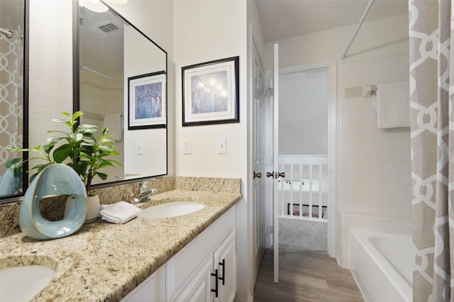 bathroom with shower / bath combination with curtain, hardwood / wood-style floors, vanity, and a textured ceiling