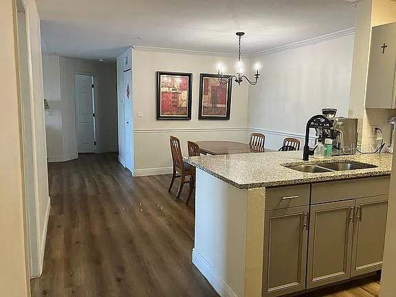 kitchen with pendant lighting, light stone counters, sink, an inviting chandelier, and dark hardwood / wood-style flooring