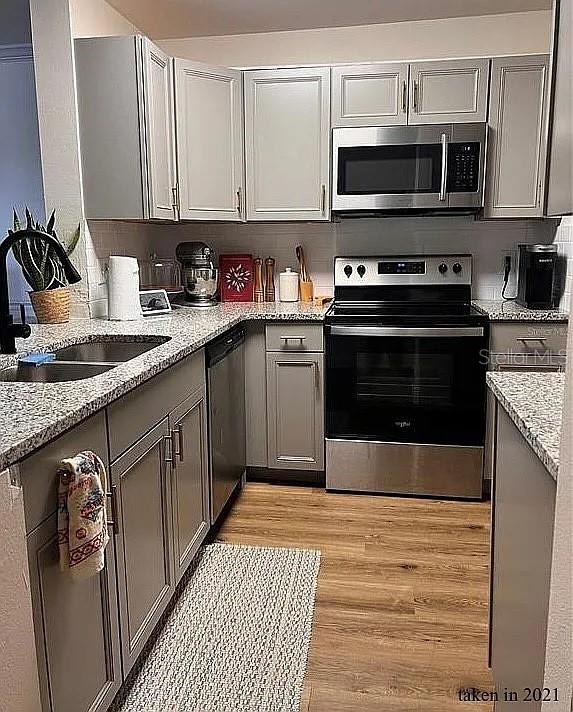 kitchen featuring gray cabinets, light wood-type flooring, light stone counters, sink, and appliances with stainless steel finishes