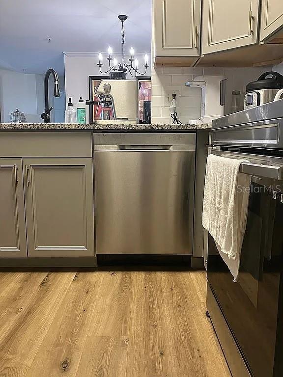 kitchen with light hardwood / wood-style floors, light stone countertops, pendant lighting, stainless steel dishwasher, and a notable chandelier