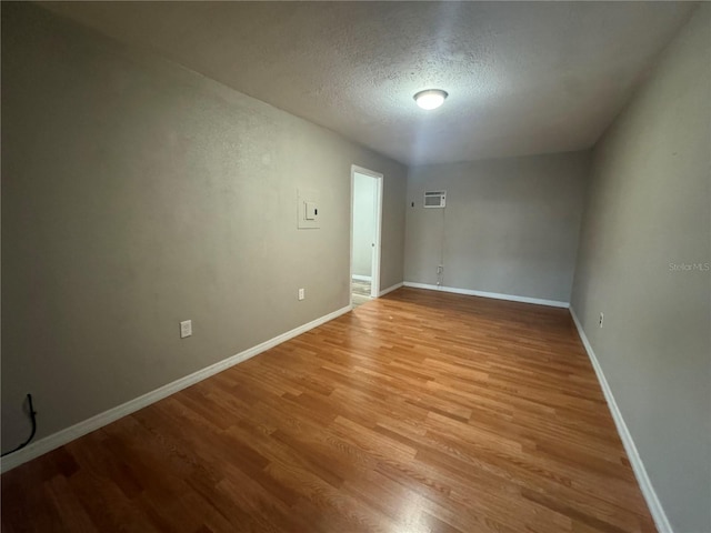 spare room featuring a textured ceiling, light hardwood / wood-style floors, and an AC wall unit