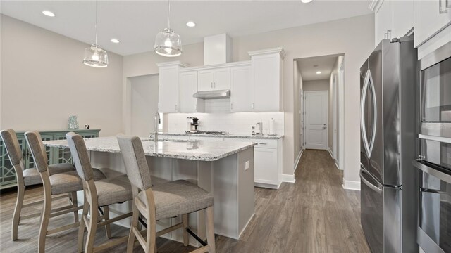 kitchen featuring appliances with stainless steel finishes, dark hardwood / wood-style flooring, pendant lighting, a center island with sink, and white cabinets