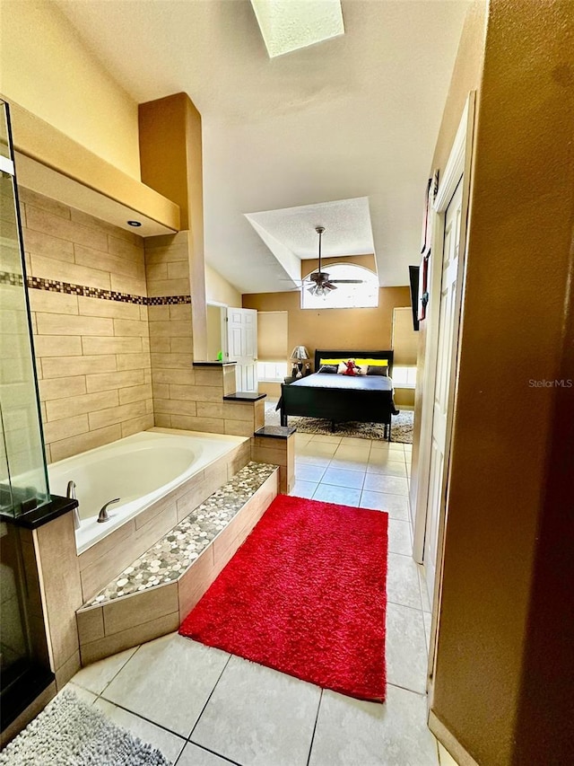 bathroom with a relaxing tiled tub, lofted ceiling with skylight, tile patterned floors, and ceiling fan