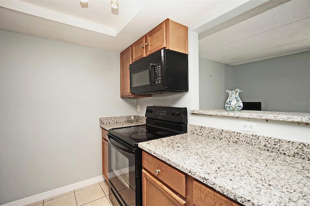 kitchen featuring brown cabinetry, light tile patterned flooring, baseboards, light stone counters, and black appliances