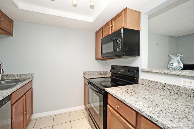 kitchen with a tray ceiling, light stone counters, sink, black appliances, and light tile patterned floors